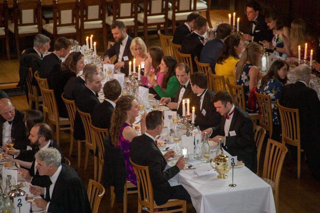 People in Black Tie at a formal dinner. The tables are covered with white clothes, there are lit candlabras, and everyone is in conversation